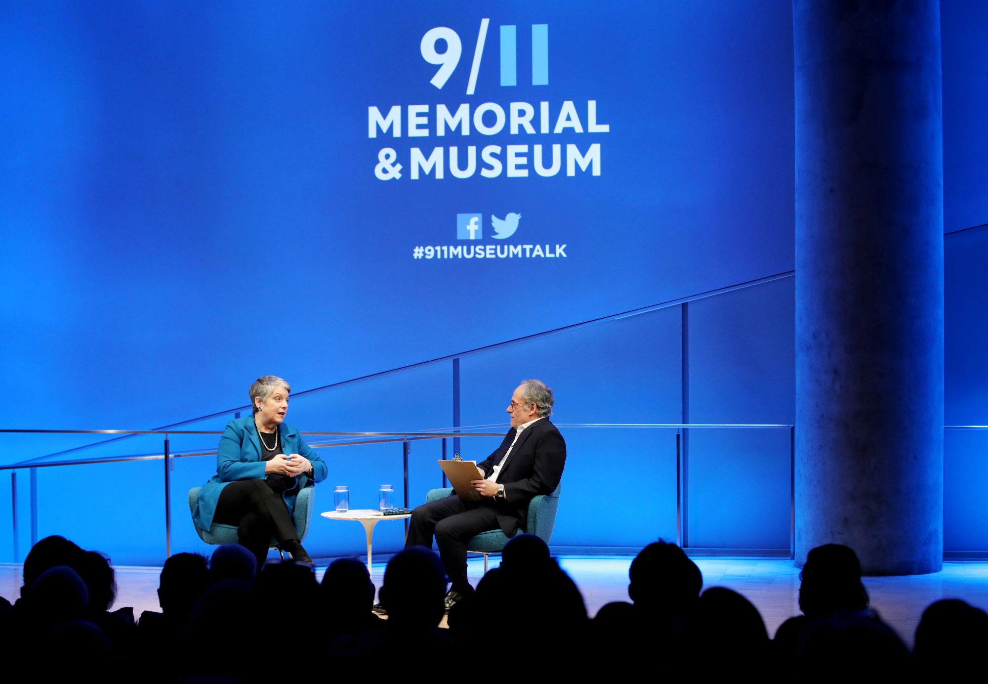 Former Secretary of the Department of Homeland Security Janet Napolitano sits beside Clifford Chanin, the executive vice president and deputy director for museum programs, during a public program in the Museum Auditorium. The photo is taken from behind the audience, which is silhouetted by the stage lights.