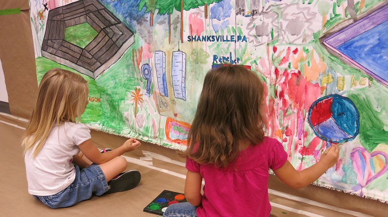 Two young girls, their hair reaching past their collars, are seen from behind as they add to a colorful hand-drawn mural honoring the victims of 9/11 in the art-making activity in the 9/11 Memorial Museum's Education Center.