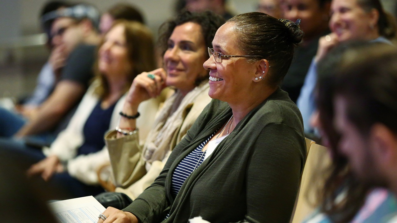 A woman smiles among an auditorium full of other educators.