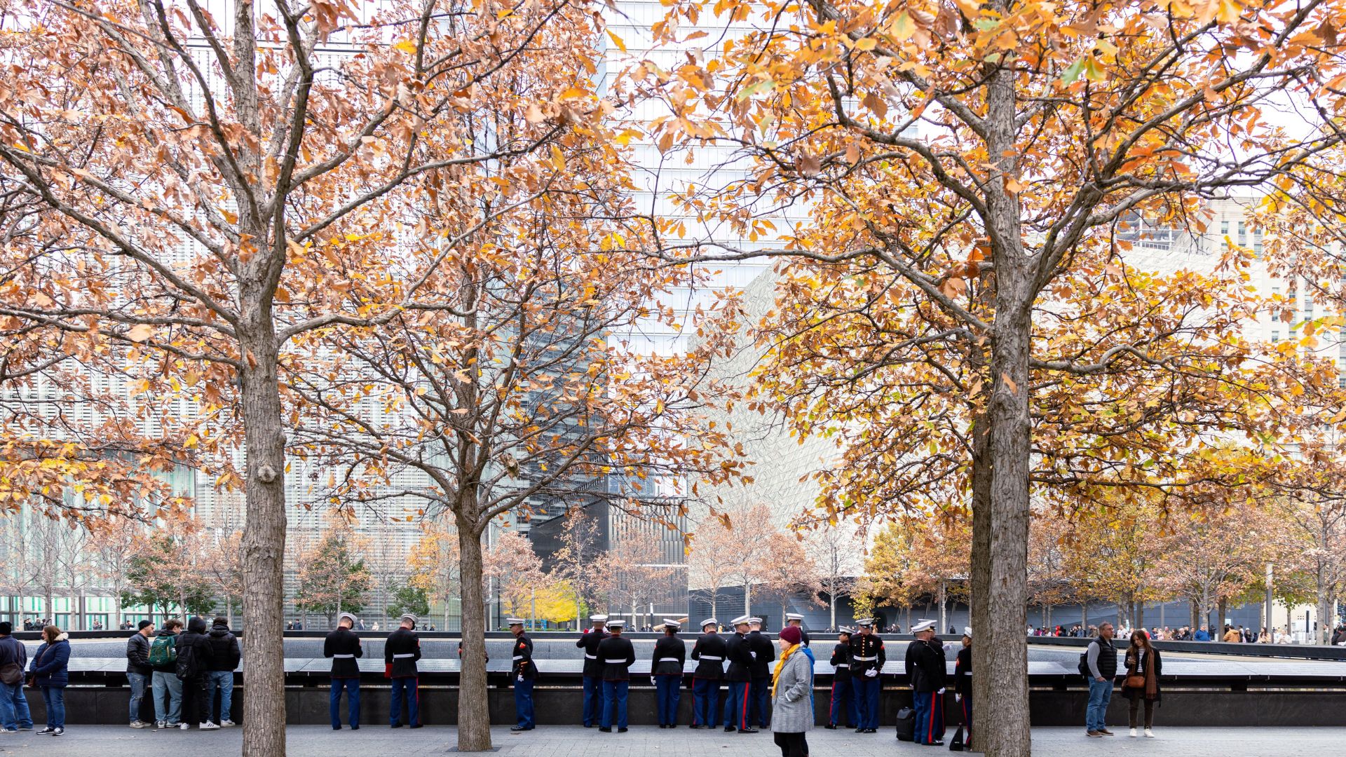 Trees covered in orange and yellow leaves line the Memorial, with U.S. sailors, Marines, and Coast Guard members in dress uniform viewing the pools