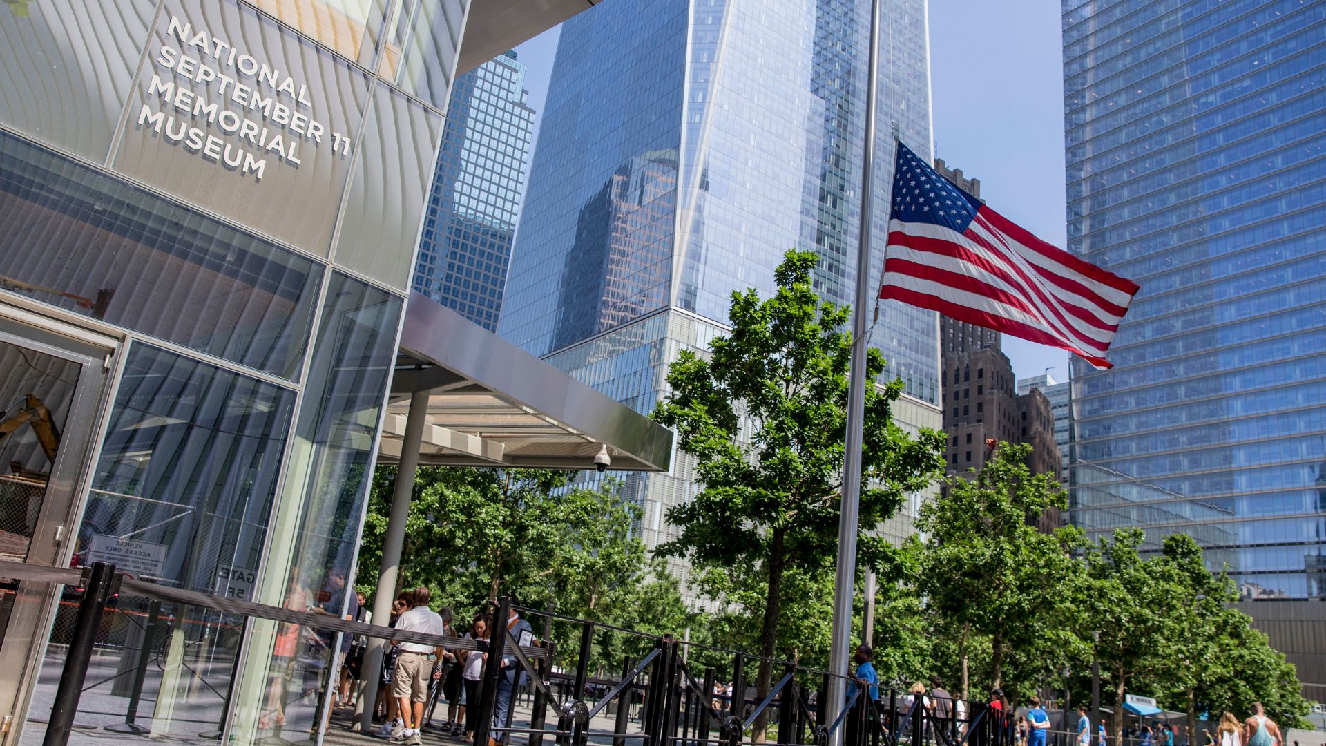 Entrance to the 9/11 Museum, with leafy green trees in the background and an American flag moving in a breeze