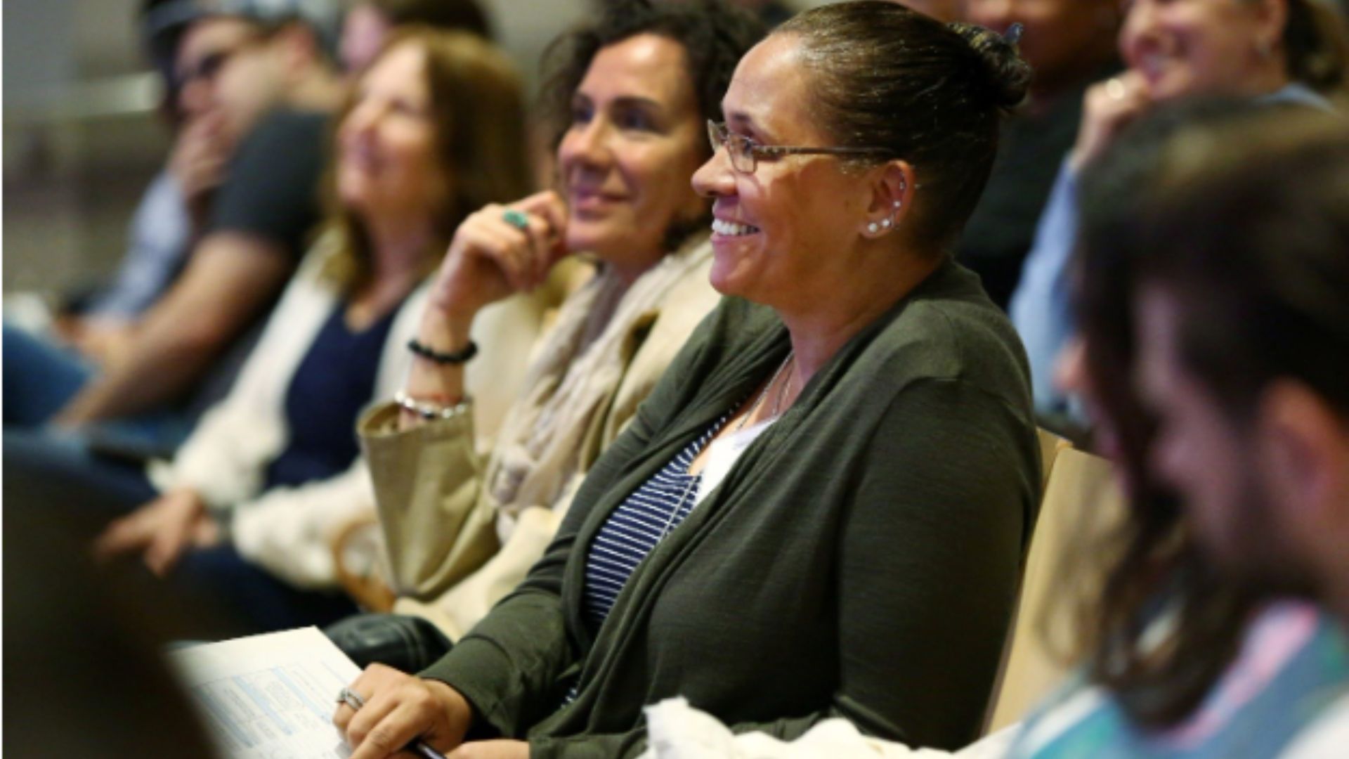 A row of people look on and listen attentively from auditorium seats