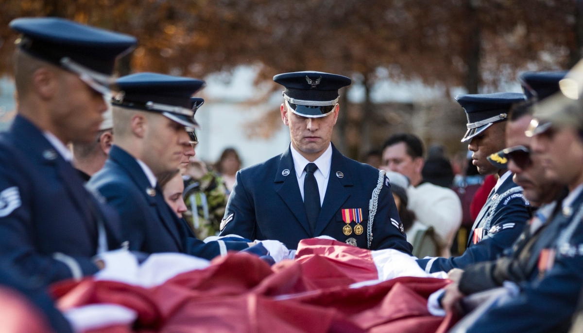 Military officers stand folding a flag.
