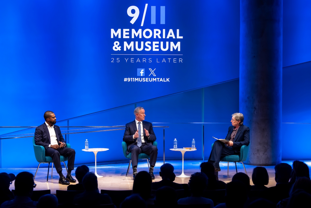 Three people sit on stage in front of a blue background 