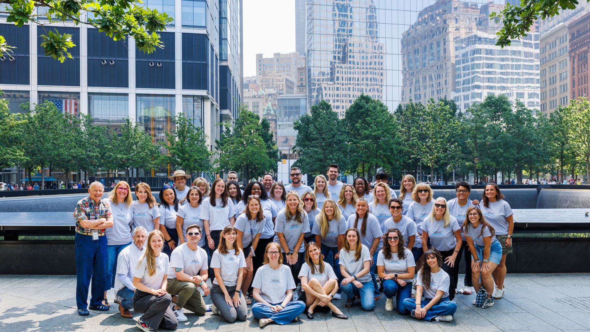 A group of adults in matching gray tee shirts pose, smiling, in three rows on the Memorial