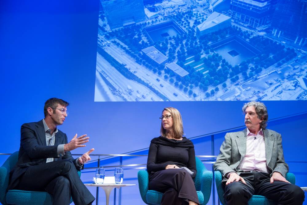 Handel Architects LLP partner Michael Arad, Paul Murdoch Architects President Paul Murdoch, and KBAS partner Julie Beckman are seen onstage with an aerial photo of the 9/11 Memorial projected on the wall behind them. Arad is speaking as Murdoch and Beckman listen to his left.