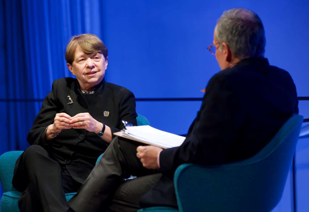 Former U.S. Attorney Mary Jo White of the Southern District of New York  gestures with her hands onstage as she speaks with Clifford Chanin, the executive vice president and deputy director for museum programs. Chanin is in the foreground and slightly out of focus as he holds a clipboard.