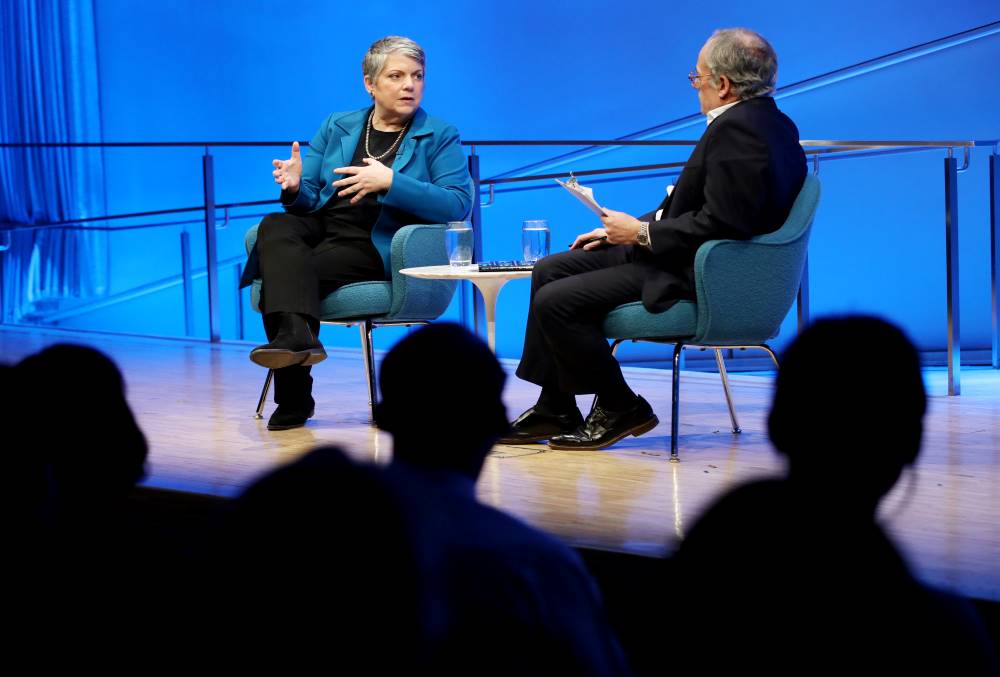 Former Secretary of the Department of Homeland Security Janet Napolitano speaks onstage as she gestures with both hands. Clifford Chanin, the executive vice president and deputy director for museum programs, listens as he sits next to her with a clipboard. The silhouettes of several audience members are visible in the foreground.