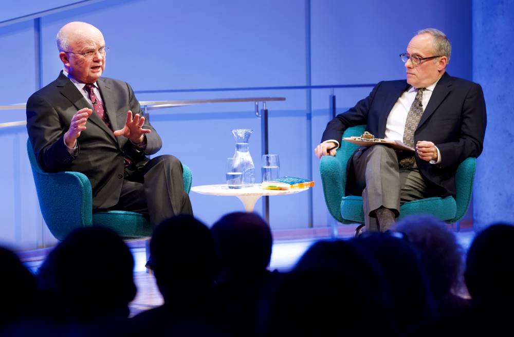 Former CIA director and retired U.S. Air Force Gen. Michael Hayden gestures onstage as part of the public program, General Michael Hayden on the War on Terror. Clifford Chanin, the executive vice president and deputy director for museum programs, listens to Hayden’s left while holding a clipboard. Members of the audience are silhouetted by the stage lights in the foreground.
