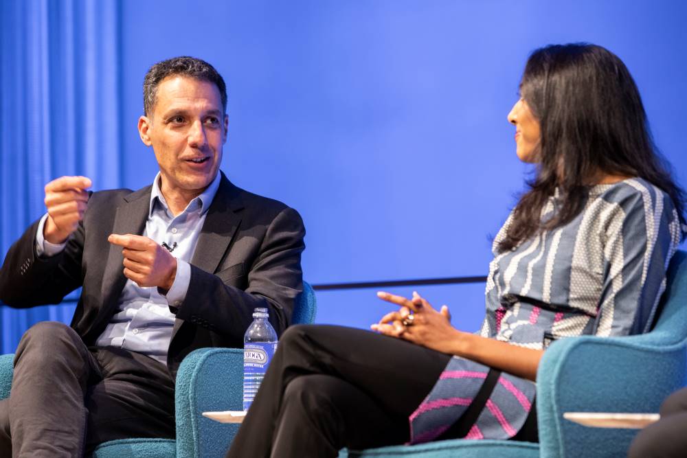Hany Farid, Dartmouth computer science professor and senior advisor to the Counter Extremism Project, gestures with both hands as he speaks onstage next to Vidhya Ramalingam, founder of Moonshot CVE, who has her hands in her lap.