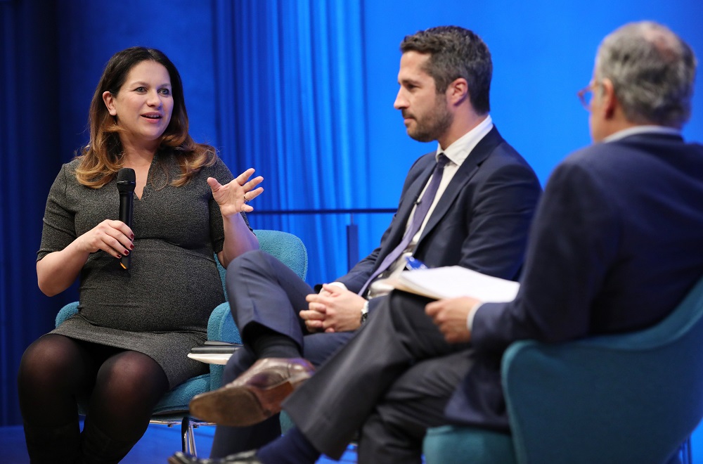 New York Times foreign correspondent Rukmini Callimachi speaks while seated onstage at the Museum Auditorium. She is holding a microphone with her right hand and gesturing with her left hand. She is looking towards Lorenzo Vidino, director of the George Washington University Program on Extremism, and Clifford Chanin, the executive vice president and deputy director for museum programs. The two men are seated next to her with their legs crossed.