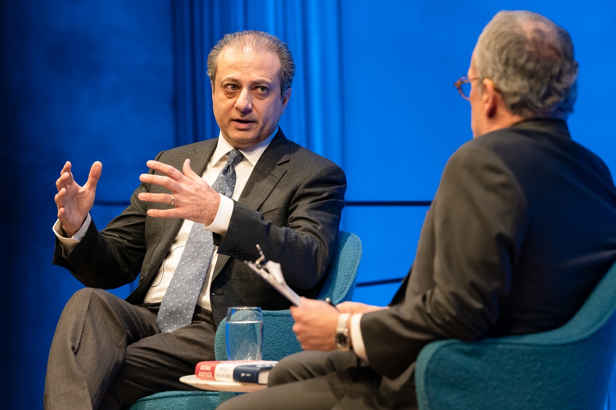 Preet Bharara, the former U.S. attorney for the Southern District of New York, gestures with both hands as he speaks with moderator Clifford Chanin. Bharara looks as if he’s explaining something to Chanin, who is looking on with a clipboard and pen in his hands.