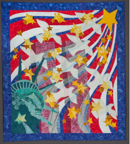 Handmade textile quilt depicts the Twin Towers at center, ghostlike in their transparency. The crowned head of the Statue of Liberty is represented in the lower left corner of the quilt, and from it white doves and yellow stars emanate. These images are set against waves of red, white, and blue. 