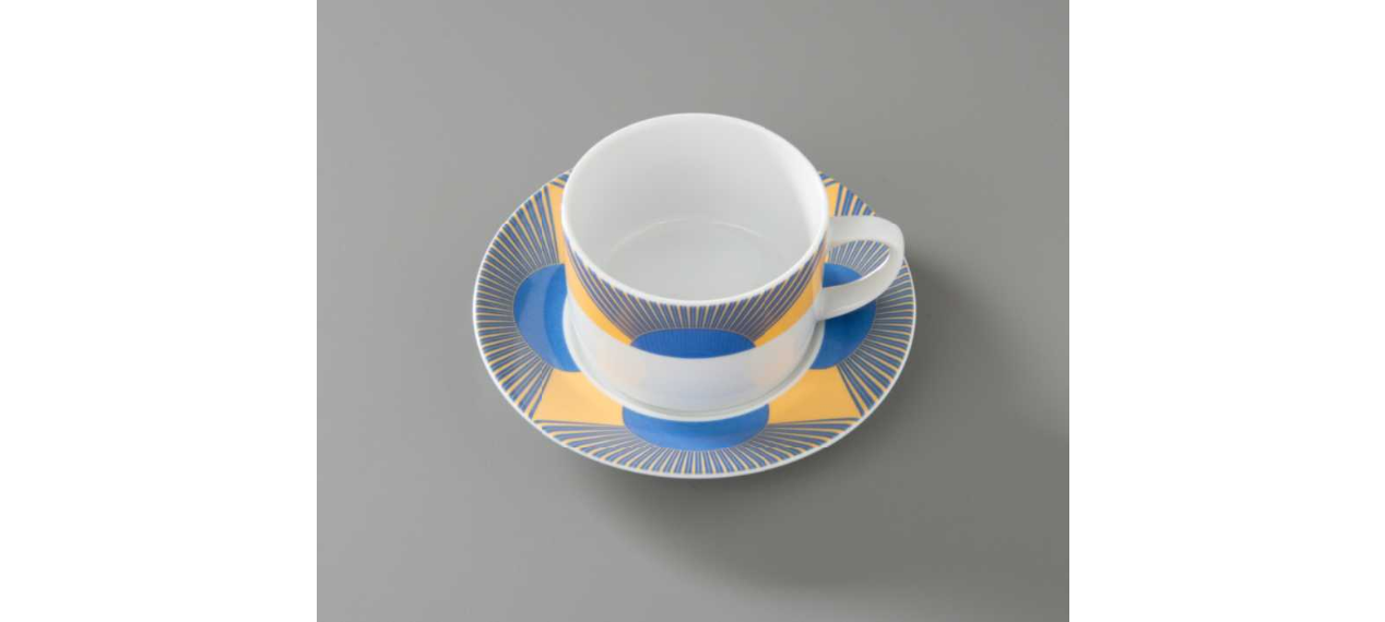 Coffee cup with matching saucer used at the Windows on the World restaurant. The yellow and blue graphic detailing resembles a rising sun, and the rays evoke the facade of the Twin Towers.