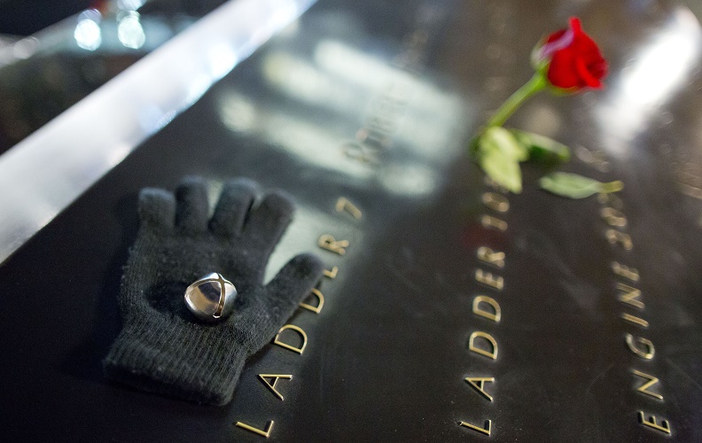 A black glove, sleigh bell, and red rose left on the 9/11 Memorial parapet at night.