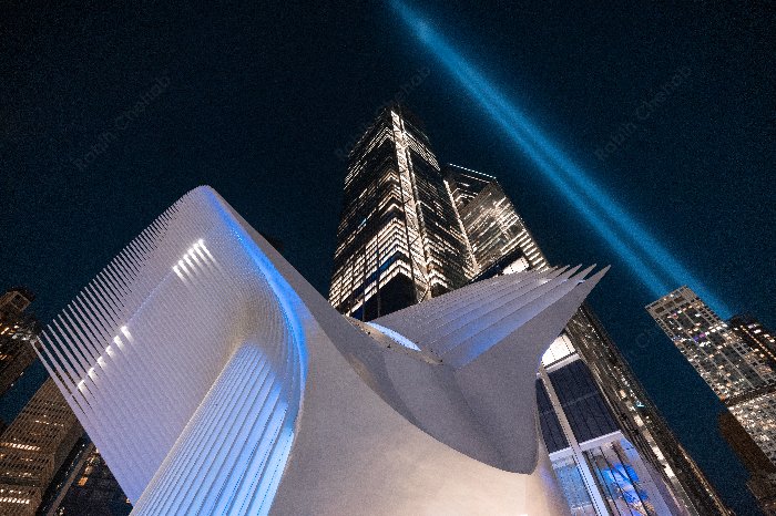 The Oculus and One World Trade Center with blue beams of light illuminating the evening sky