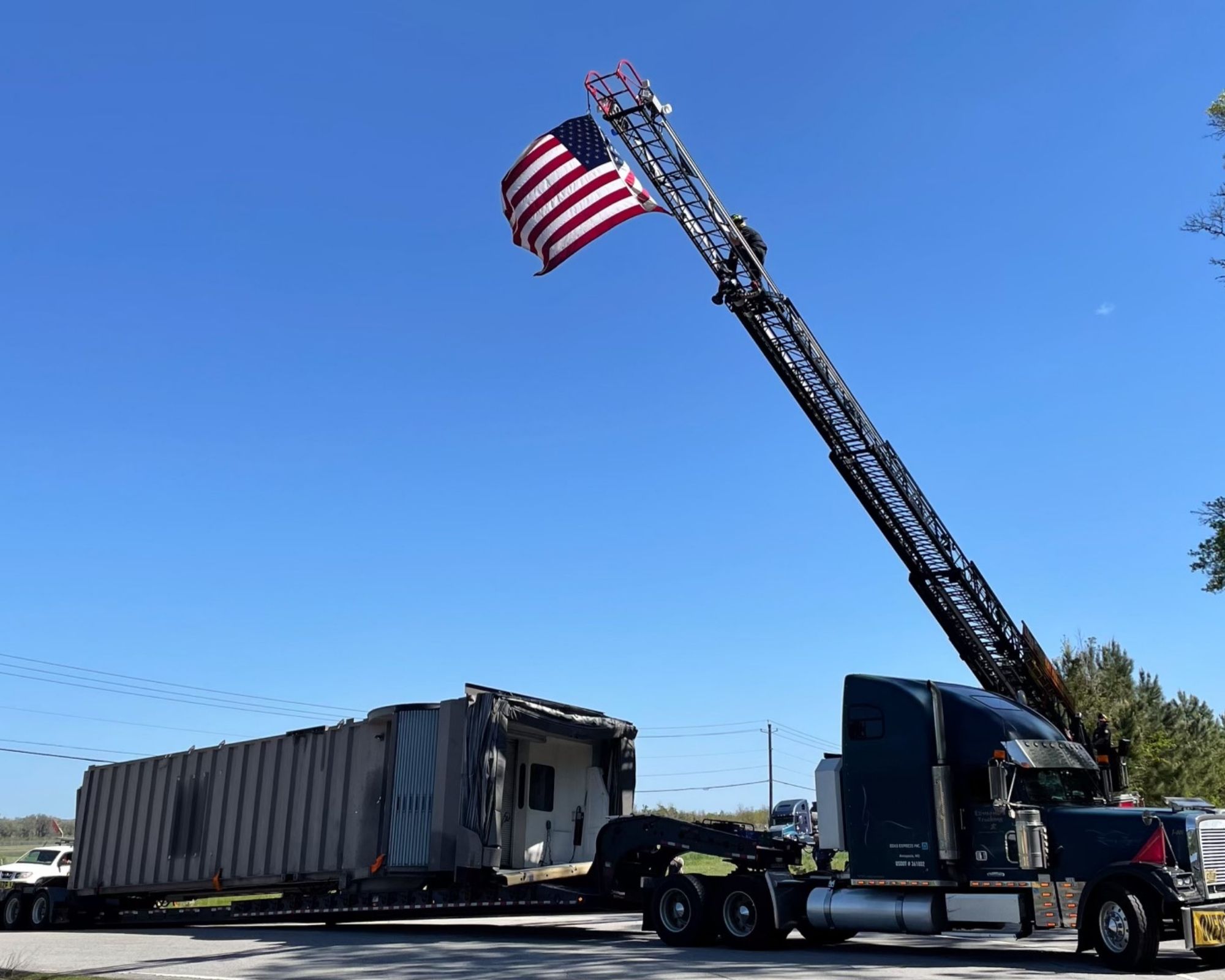 A crane raises the American flag over the jetway, which appears on the bed of a large truck