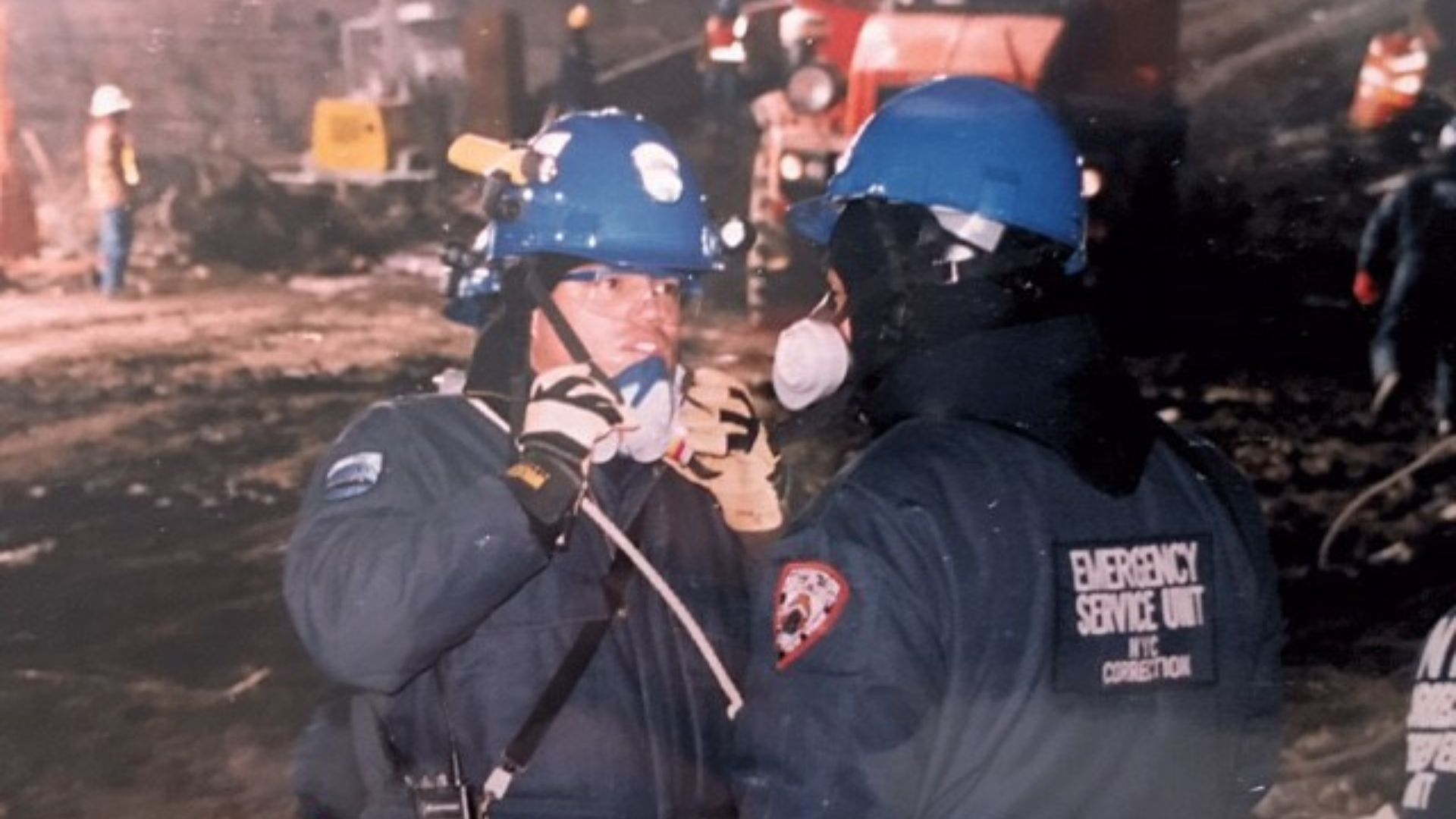 Two men in Department of Correction gear speak at Ground Zero. The man on the left has a face mask pulled down.