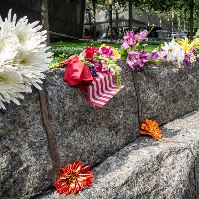 flowers and an American flag adorn a stone and steel monolith