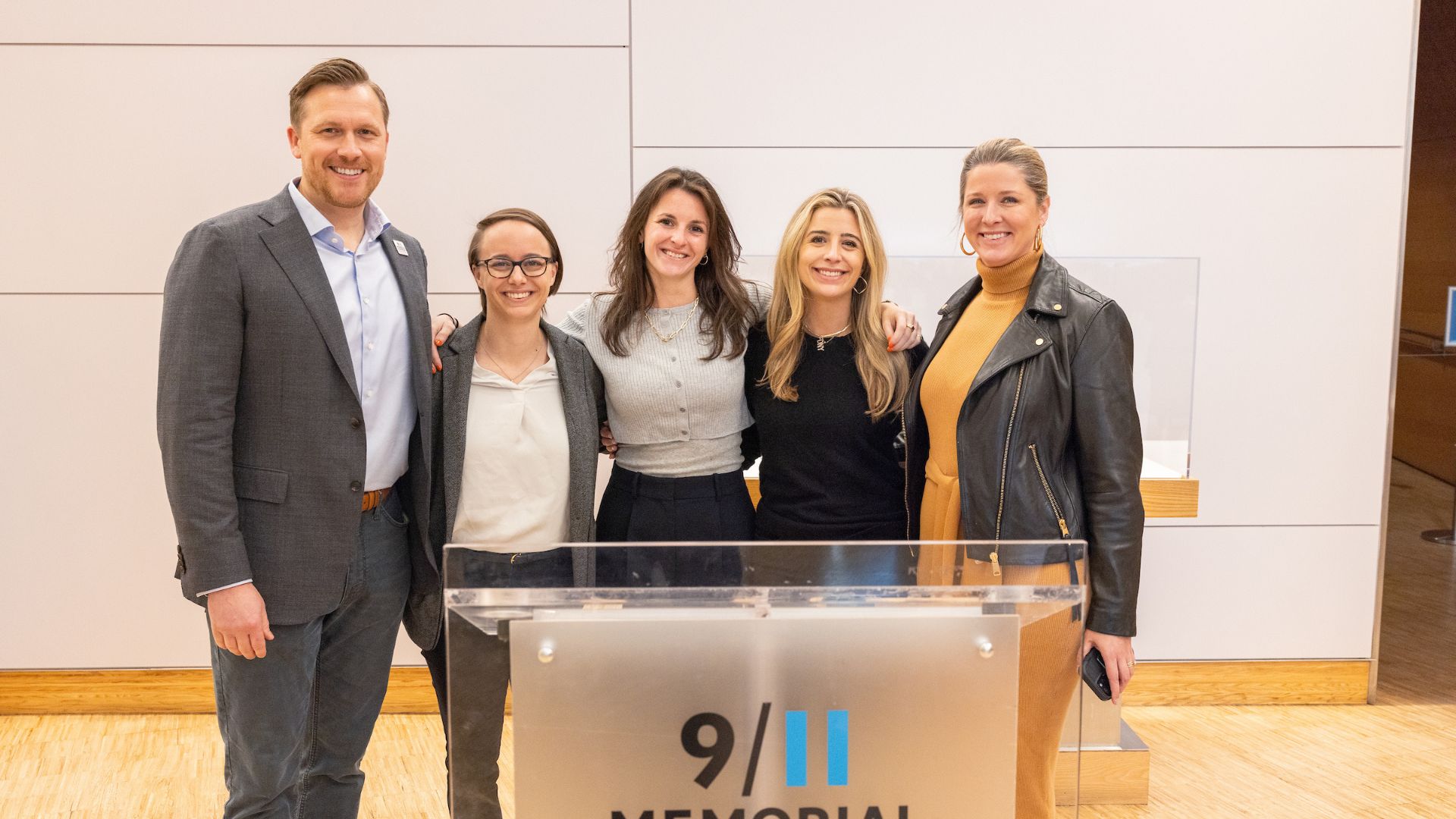 Five smiling people at a 9/11 Memorial podium inside the Museum