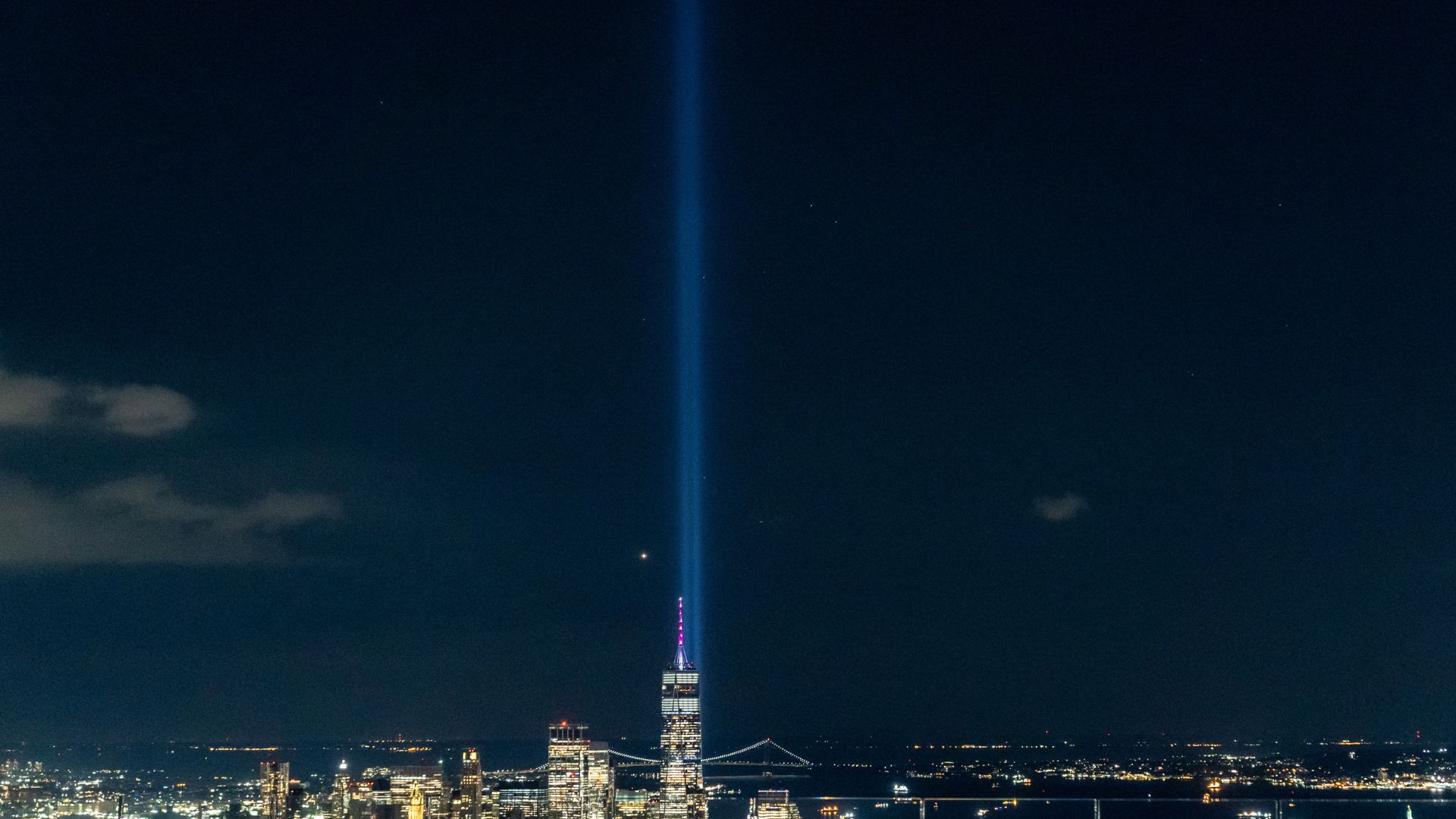 Twin beams of light illuminate the dark blue evening sky with New York City skyline in background