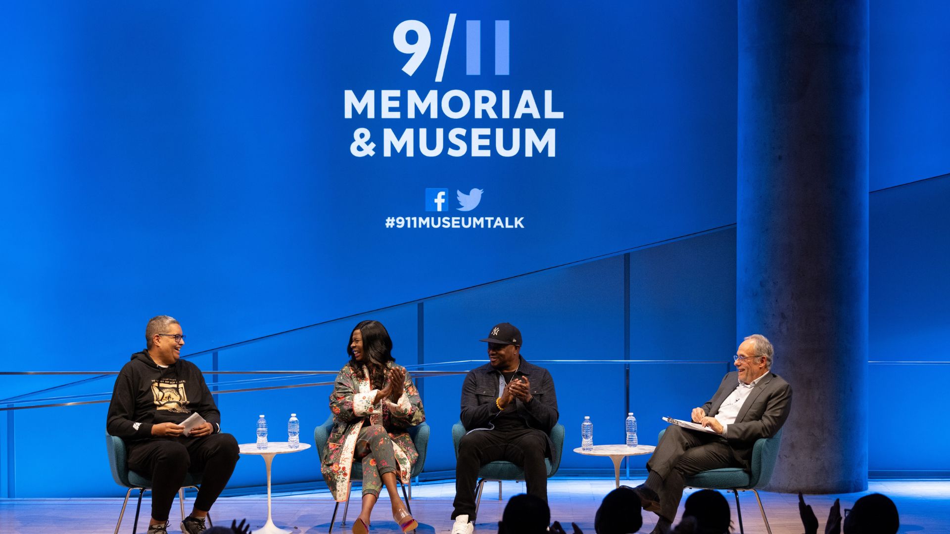 Four speakers on stage during a panel discussion at the Museum, in front of a screen bearing the 9/11 Memorial & Museum logo