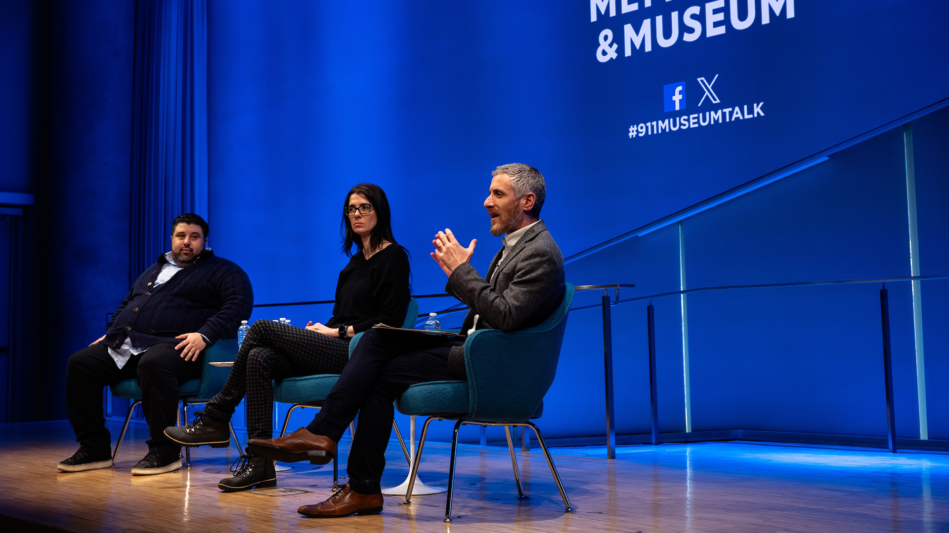 Three speakers, sitting on stage against a blue background displaying the 9/11 Memorial and Museum logo.
