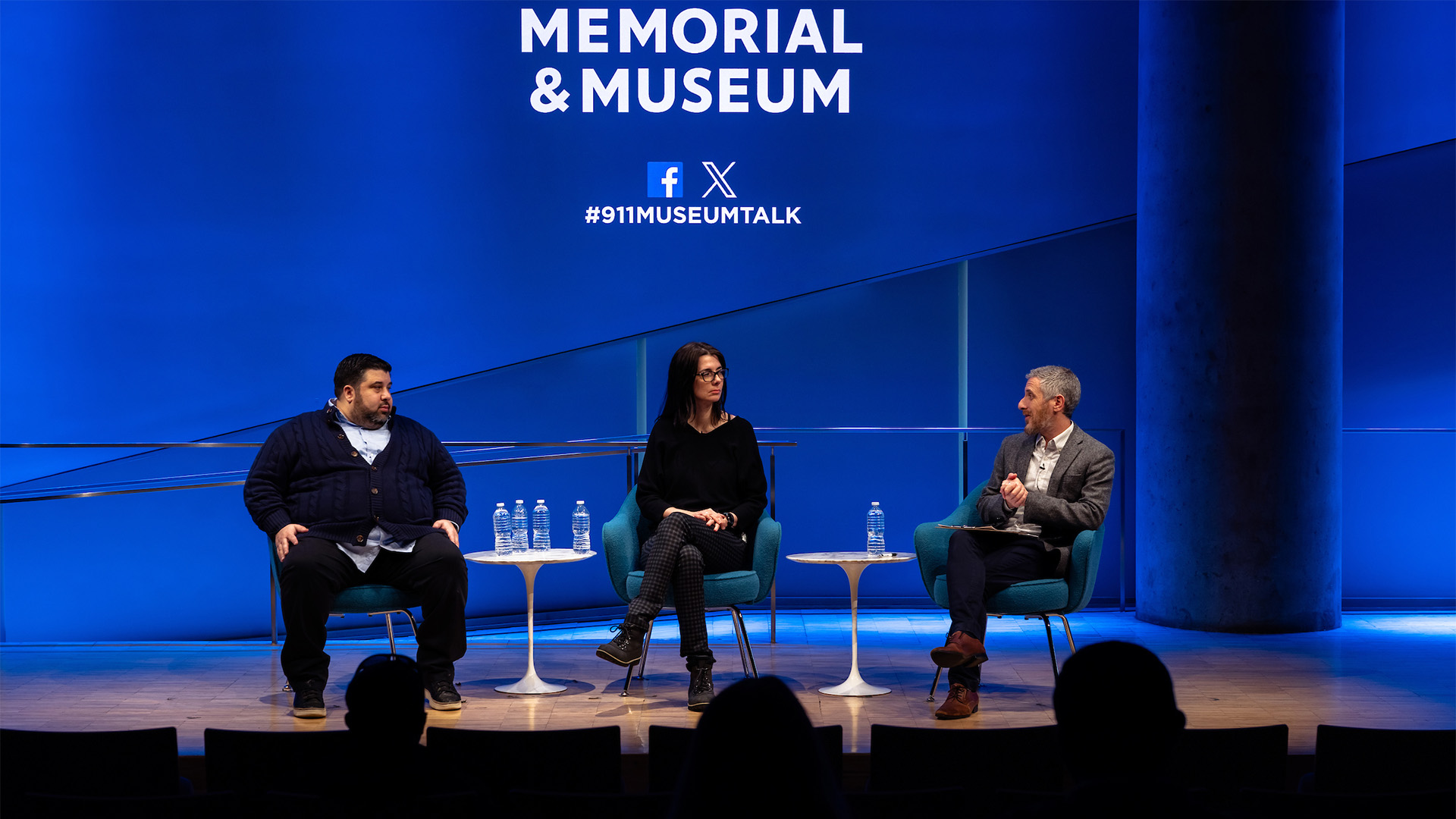 Three speakers, sitting on stage against a blue background displaying the 9/11 Memorial and Museum logo.