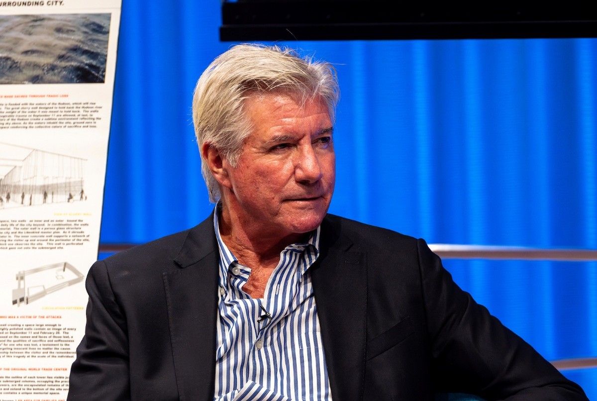 A man in a jacket faces a speaker off camera and listens intently