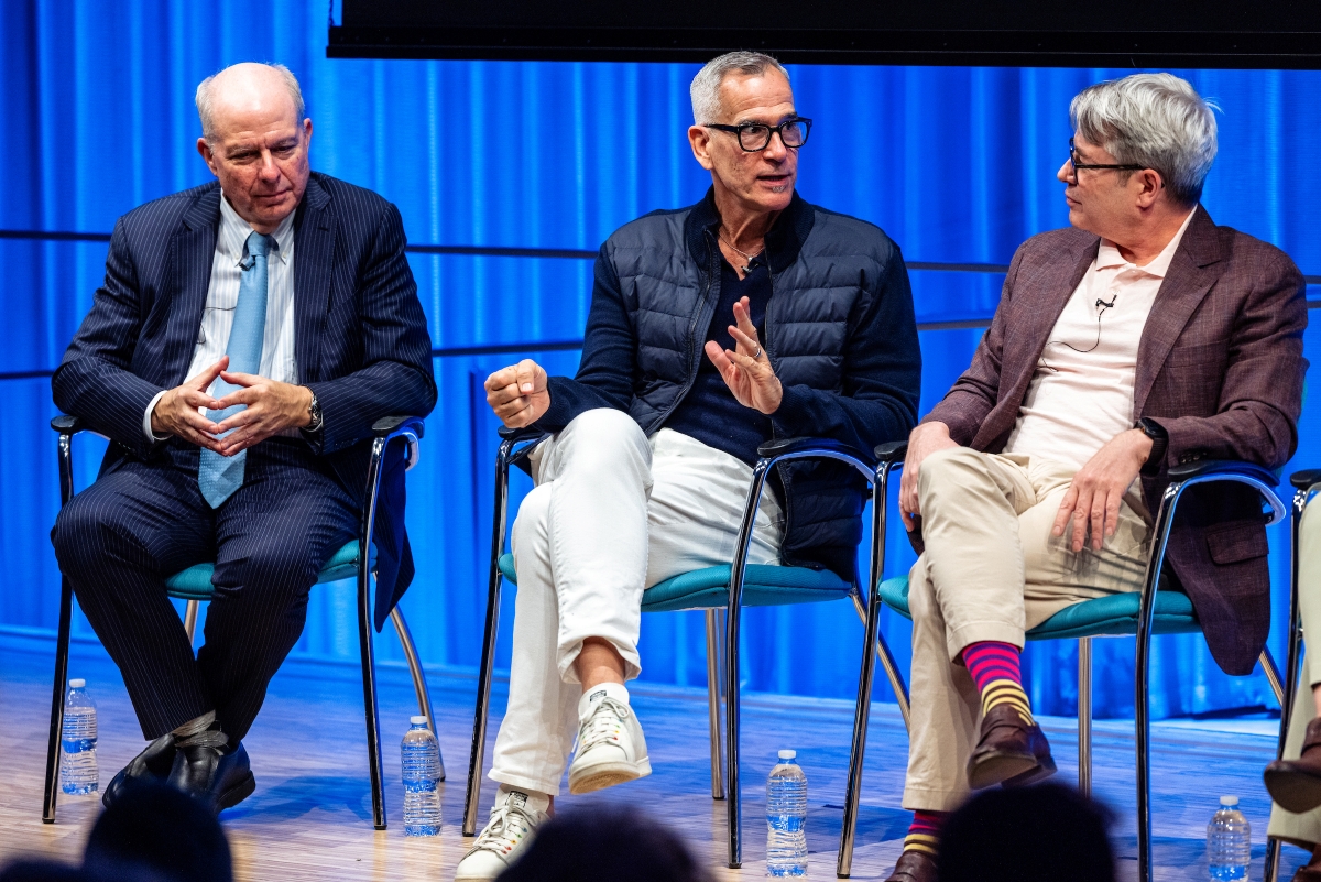 Three speakers sit on stage, engaged in conversation