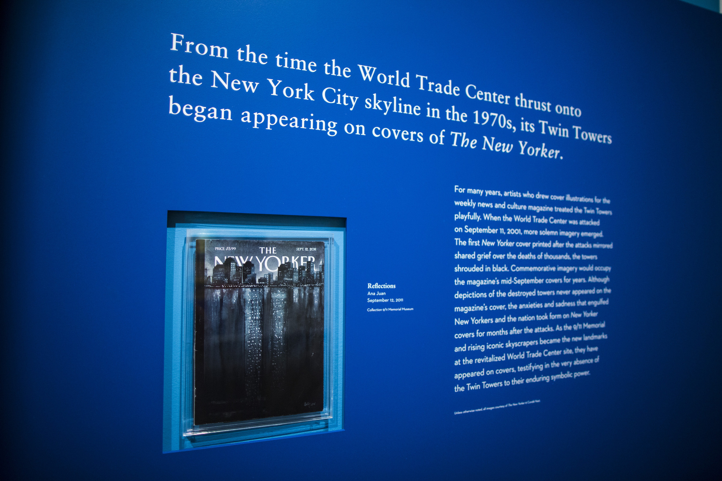 A blue wall features a recessed mounted New Yorker magazine cover showing the Twin Towers alongside wall text about the exhibition "Cover Stories." 