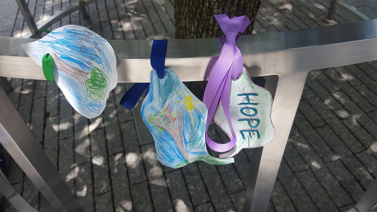 Three pieces of papers colored by children, cut into the shape of leaves, and tied with ribbons to a metal railing. 