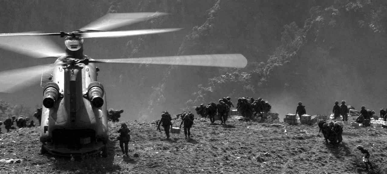 Back view of soldiers carrying supplies from a helicopter on mountaintops. 
