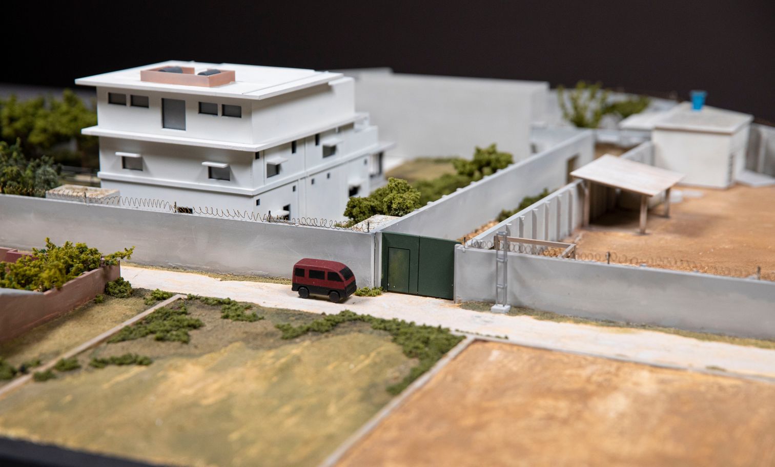 Aerial view of model of a walled white compound surrounded by predominantly brown landscape. 