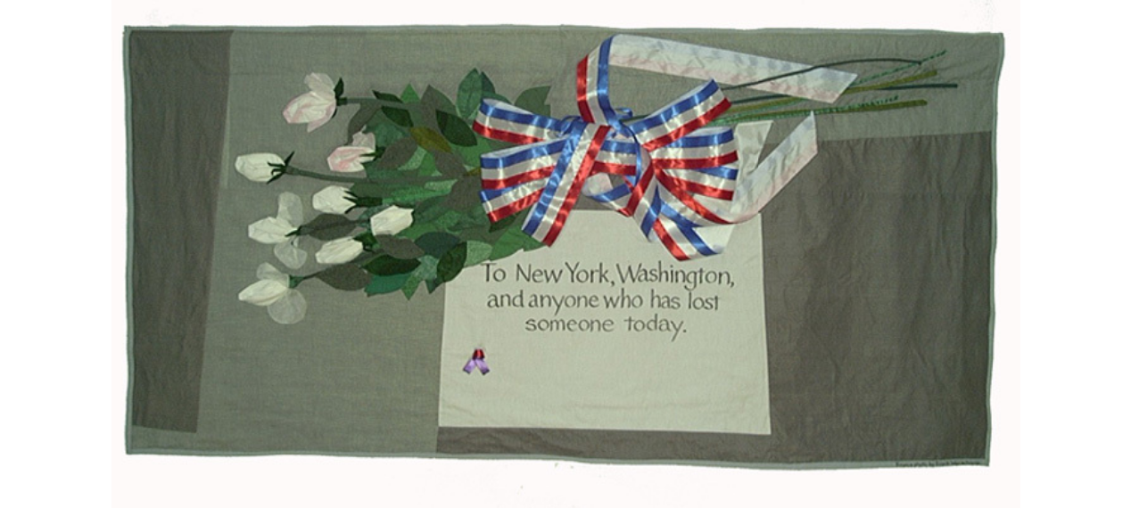 This quilt depicts a bouquet of white roses tied together with a red, white, and blue ribbon. The backing fabric is gray to represent the sidewalk, and the white patch in the center is a note with text: "To New York, Washington, and anyone who has lost someone today." 