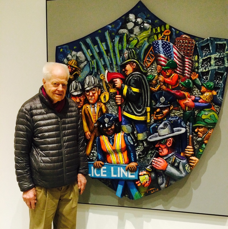 The artist, wearing a black puffer jacket, stands in front of "The Shield" hanging in the 9/11 Memorial Museum. 