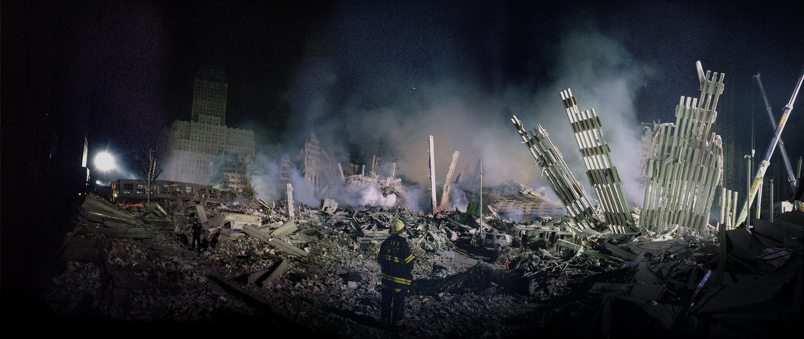 A lone FDNY firefighter stands among the Ground Zero ruins at night.