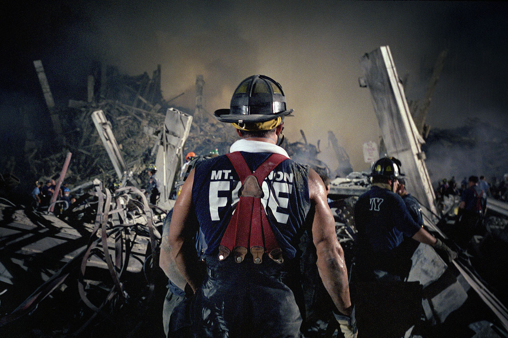 The back of a firefighter, in a Mt. Vernon Fire t-shirt, at Ground Zero at night.