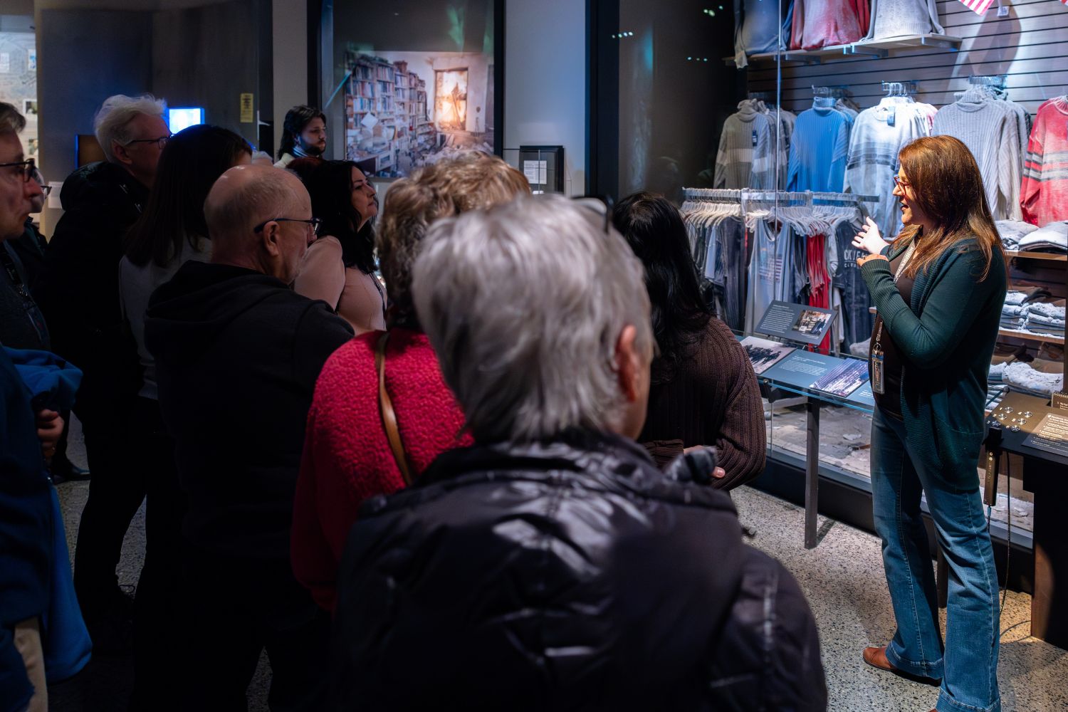 a tour guide stands facing a group in the Museum Store, back to a wall of merchandise