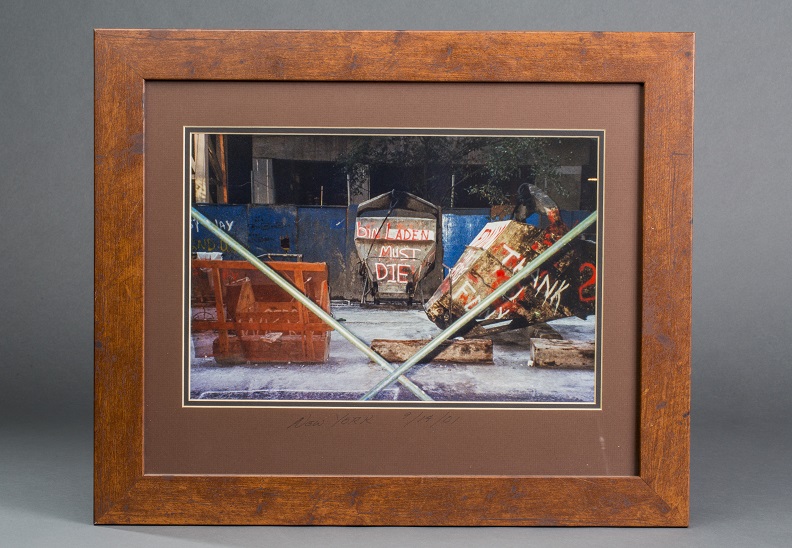 Framed photograph depicting construction fence with graffiti on it.