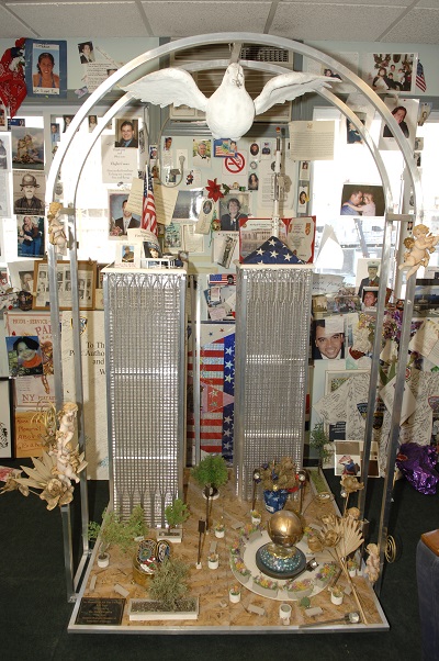 Grijalva's Twin Tower sculpture stands in the 9/11 Family trailer, foregrounding a wall covered in photos of deceased family members.