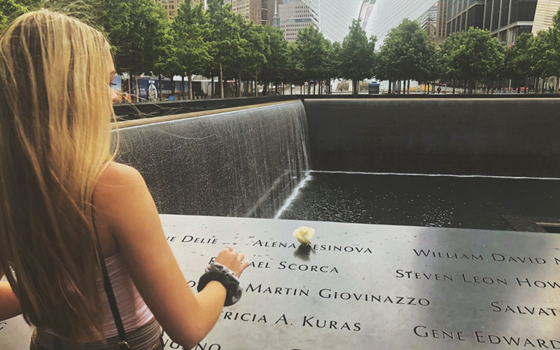 The back view of a blonde young woman placing a flower on the 9/11 Memorial