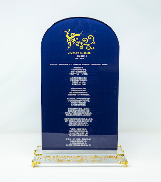 A navy blue glass plaque, rounded on top, with gold and white lettering in Chinese, sits on a clear glass base with gold feet.
