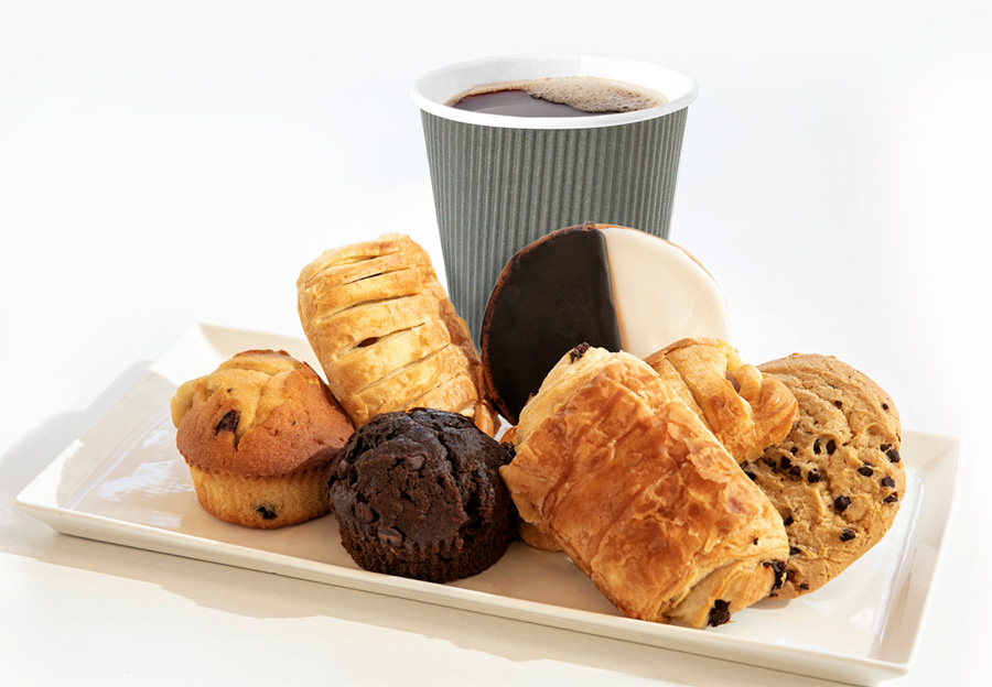 Cup of coffee on tray, surrounded by assorted pastries