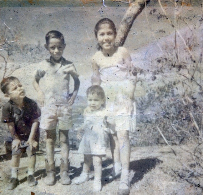 Grainy image of four children wearing summer clothes, in front of tree branches