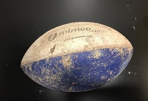 A worn and dusty white and blue foam football from the 9/11 Memorial Museum's collection rests on a black surface.