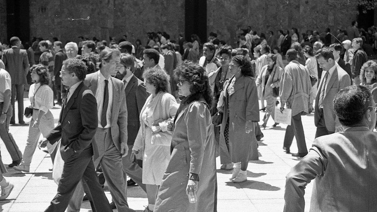Black and white image of a crowd of people walking leftward.