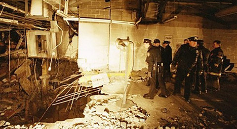 Officers inspecting the crater left by the blast. The officers are standing to the right and looking down at twisted rebar and crumbled concrete to the left.