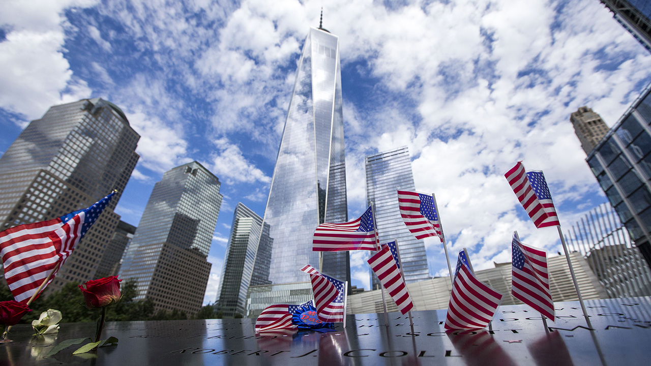Skyline surrounding the Memorial pools, with American flags in parapet and a cloudy blue sky in background