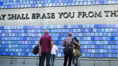 Five Museum visitors stand with their backs to the camera in Memorial Hall, observing two site-specific artworks. A quotation forged from recovered World Trade Center —“No day shall erase you from the memory of time”—speaks to the Museum’s promise to remember the 2,983 lives lost on 9/11 and in the 1993 bombing. Surrounding the letters of the Virgil quote is a work by artist Spencer Finch titled Trying to Remember the Color of the Sky on That September Morning. 